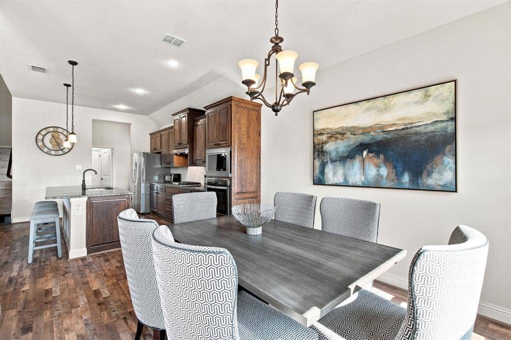 Wood-finish flooring throughout, kitchen with dark wood cabinetry and stainless steel appliances, kitchen island with built-in sink, recessed lighting, and an ornate chandelier