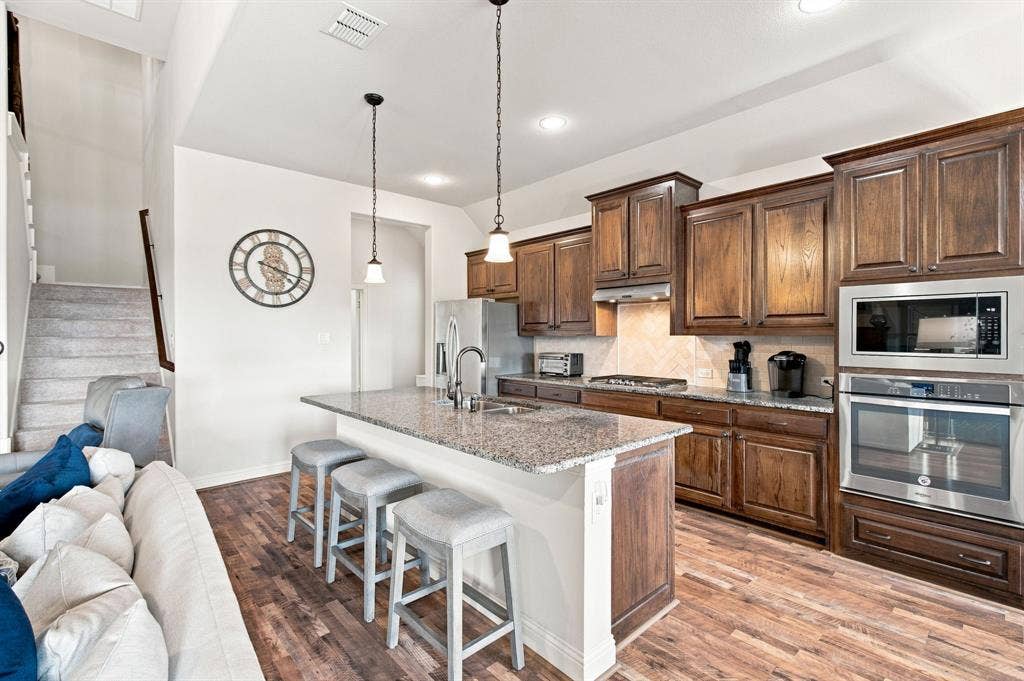Kitchen featuring wood-finish flooring, granite countertops, wood cabinetry, and stainless steel appliances