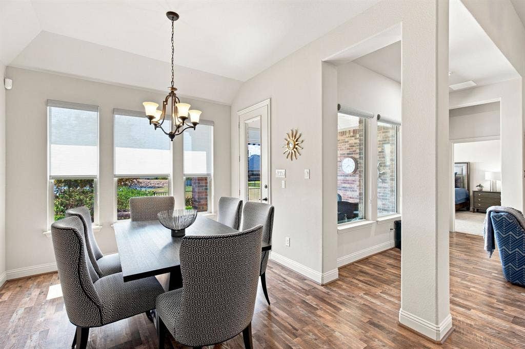 Wood-finish flooring, multiple windows with roller shades, a traditional chandelier, and architectural columns