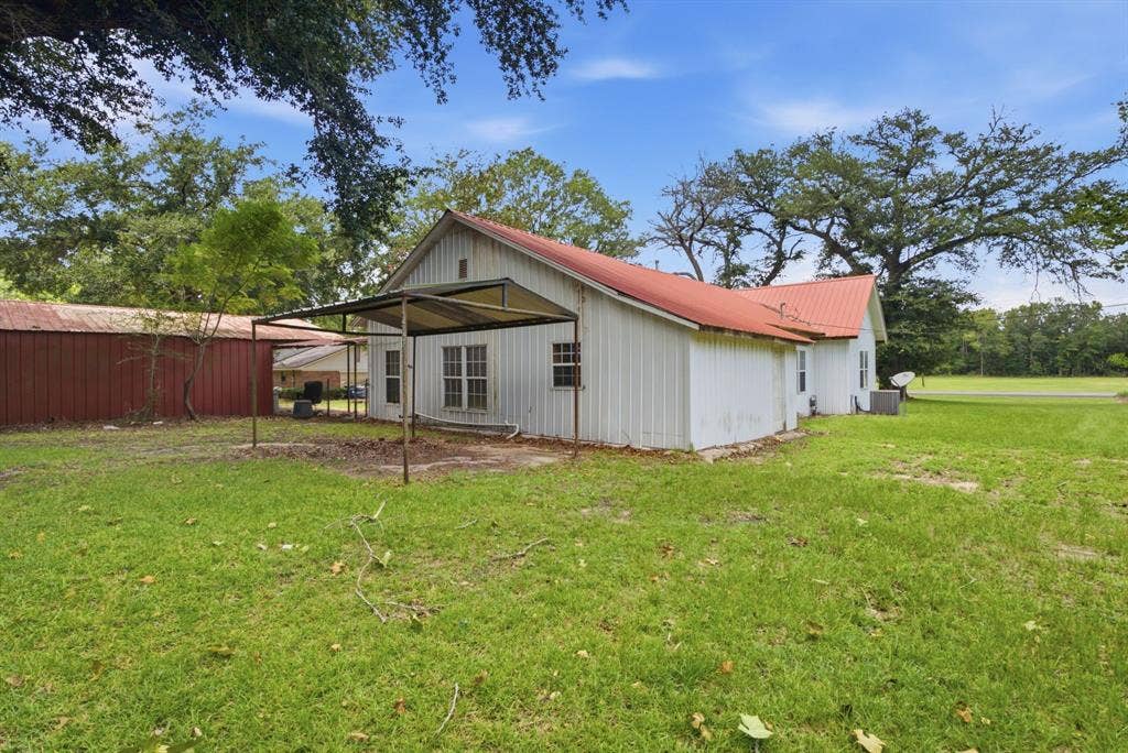 506 E Longview Street, Arp, TX 75750 Expansive grassy yard with mature trees, a red metal roof, white siding, and a covered patio structure