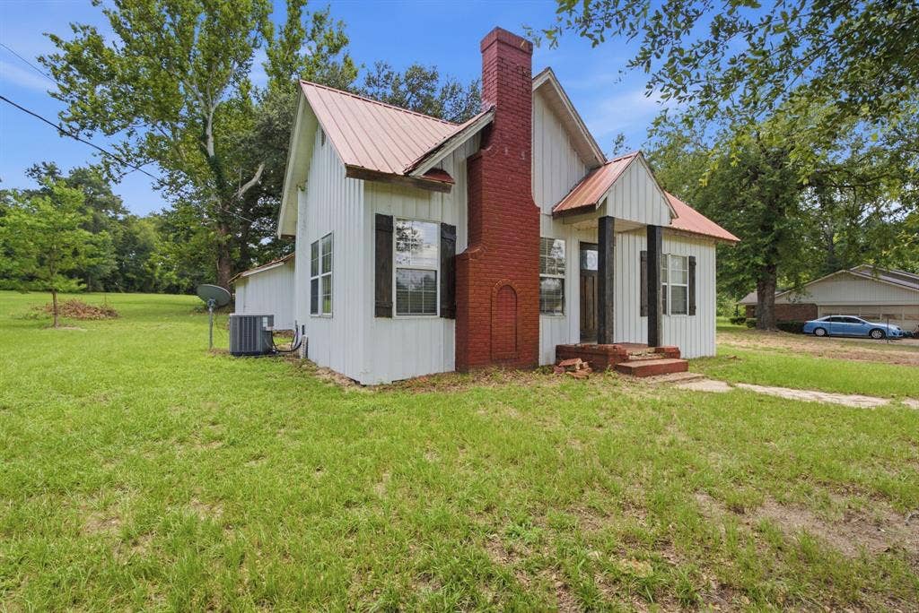 506 E Longview Street, Arp, TX 75750 White vertical siding exterior with a red metal roof, a prominent brick chimney, and a covered entry