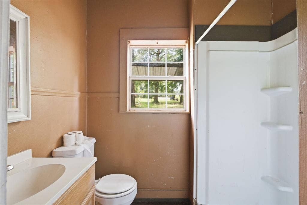 506 E Longview Street, Arp, TX 75750 Bathroom featuring a vanity with an integrated sink, a toilet, a window with exterior views, and a white shower stall with built-in shelving
