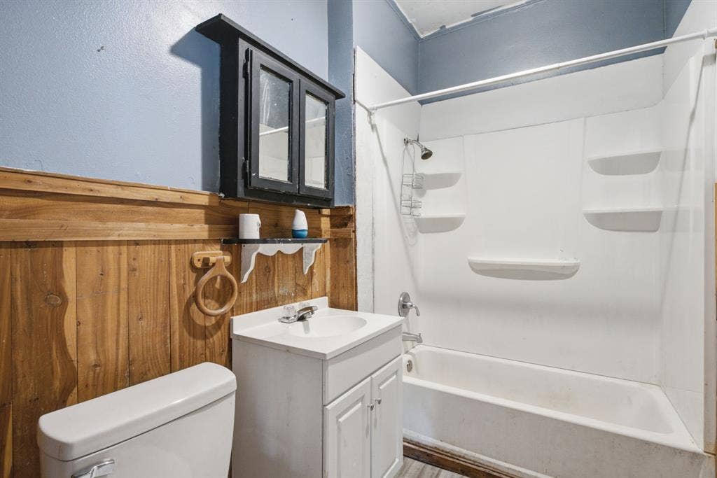 506 E Longview Street, Arp, TX 75750 Wall-mounted black medicine cabinet, wood-finish wainscoting, white vanity with integrated sink, white toilet, and a white shower-over-tub unit