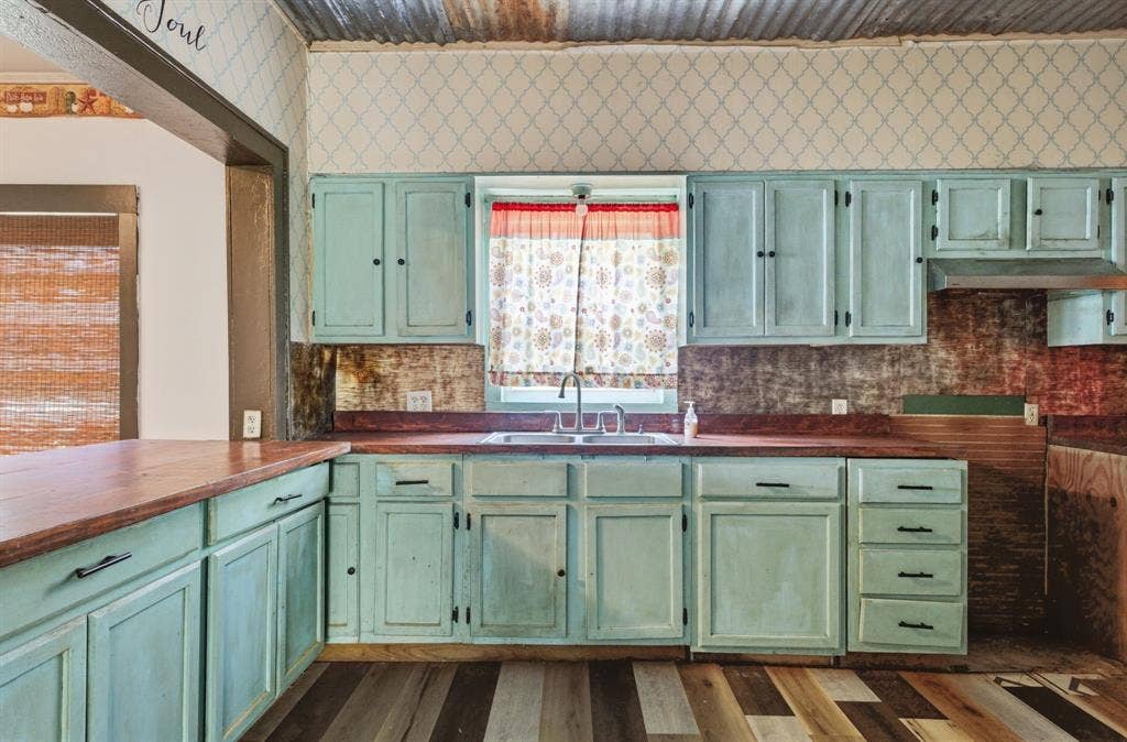 506 E Longview Street, Arp, TX 75750 Kitchen featuring distressed blue cabinetry, wood-finish countertops, stainless steel sink, a corrugated metal ceiling, and patterned wallpaper