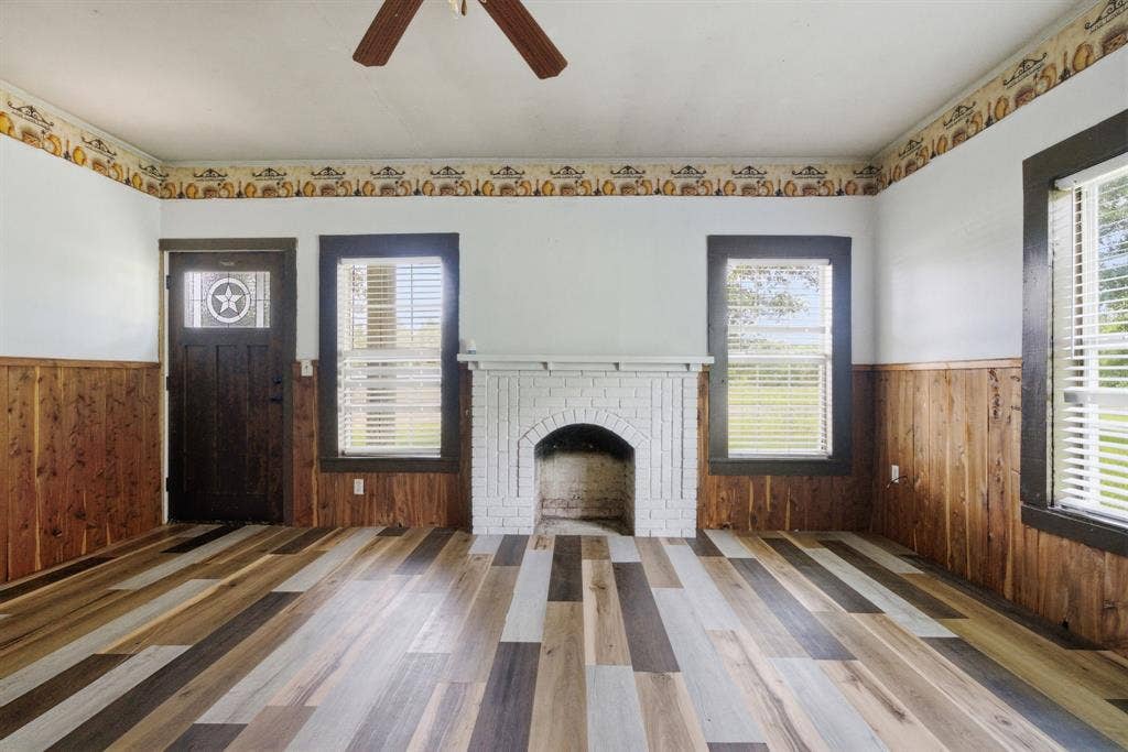 506 E Longview Street, Arp, TX 75750 Multi-tone wood-finish flooring, white brick fireplace, wood wainscoting, and a ceiling fan