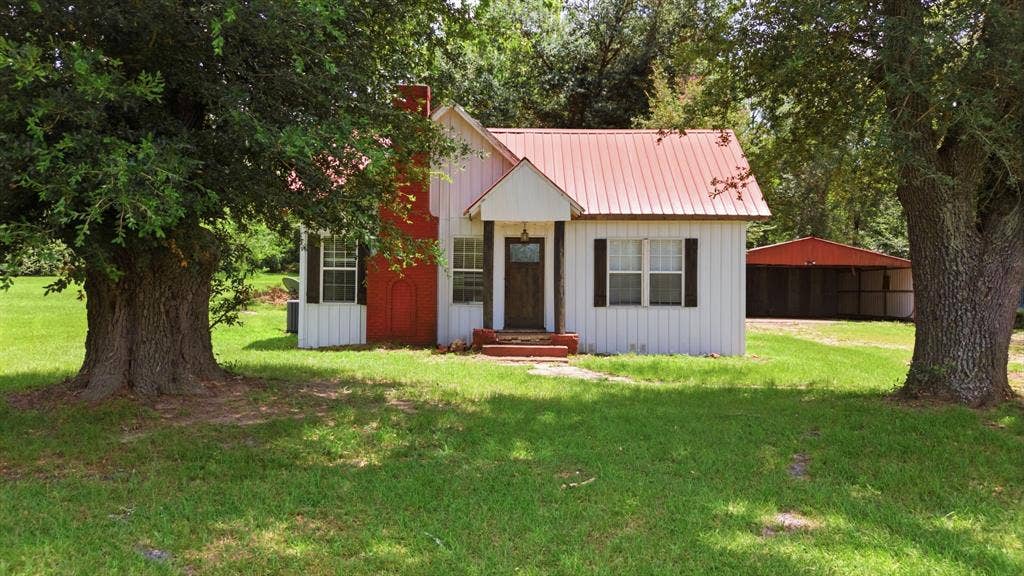 506 E Longview Street, Arp, TX 75750 White siding exterior with a red metal roof, chimney, and dark wood shutters