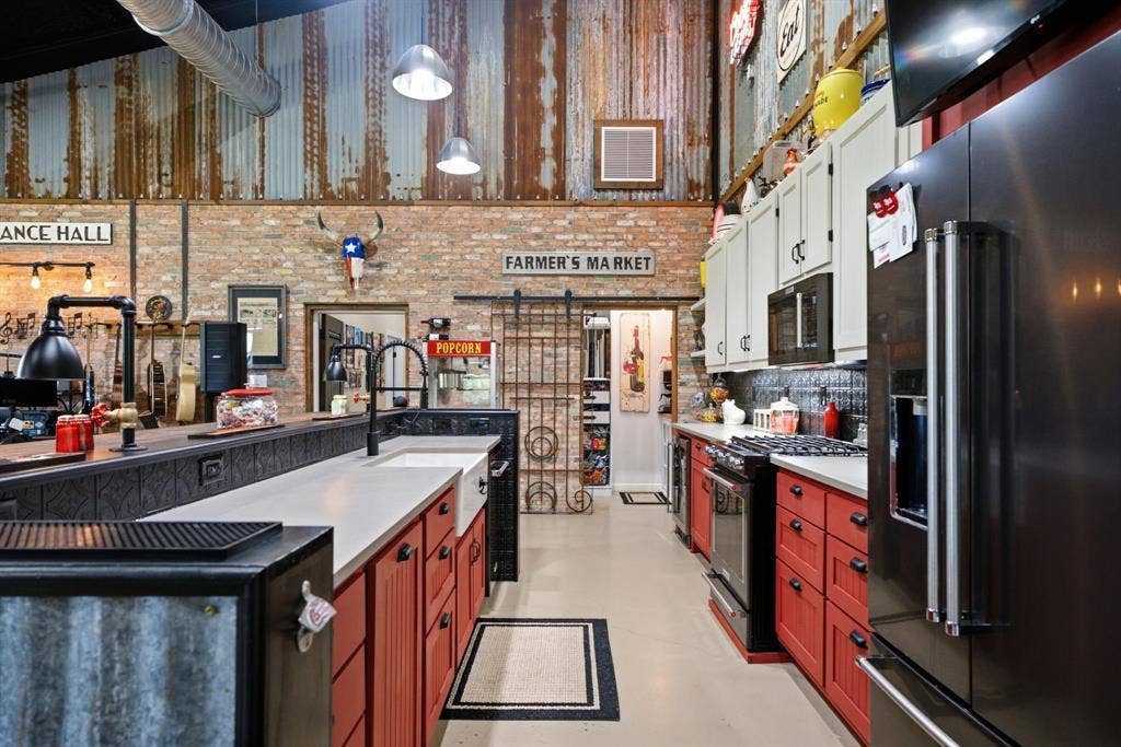 12842 Farm to Market 838, Overton, TX 75684 Industrial-inspired kitchen featuring red cabinetry with black countertops, stainless steel appliances, exposed brick walls with shiplap detailing, pendant lighting, and polished concrete flooring throughout the open layout