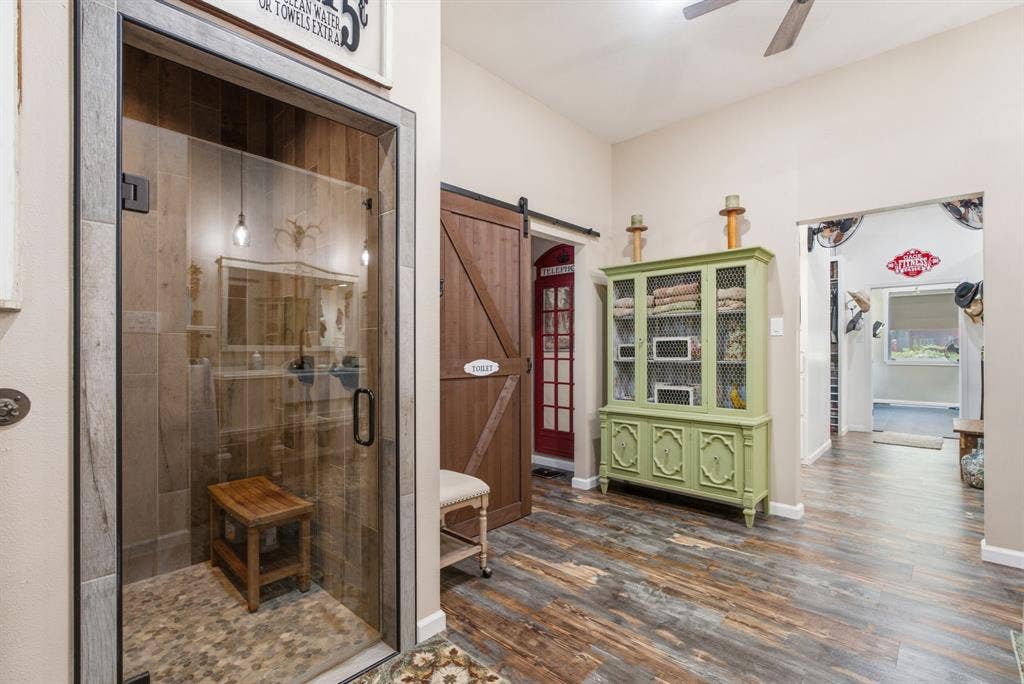 12842 Farm to Market 838, Overton, TX 75684 Primary bathroom suite showcasing a custom walk-in shower with wood-finish barn door, stone tile surround, and integrated bench seating