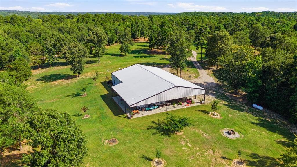 12842 Farm to Market 838, Overton, TX 75684 Metal-sided structure with a covered porch, expansive green space, and a gravel drive