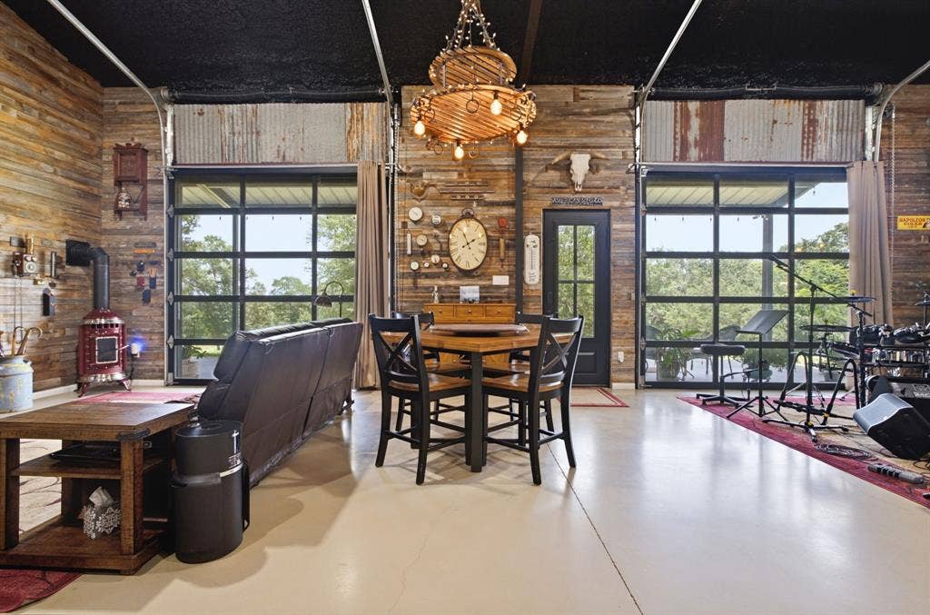 12842 Farm to Market 838, Overton, TX 75684 High ceilings with exposed ductwork, wood panel accent walls, large glass garage door, wood-finish flooring, and built-in wood-burning stove