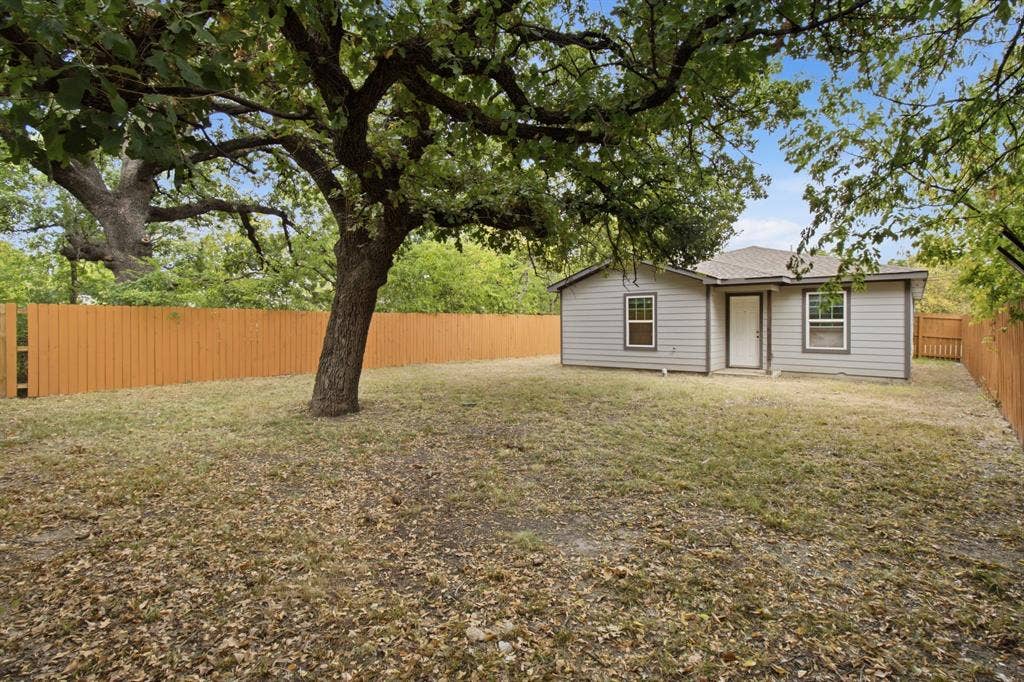 3923 Metropolitan Avenue, Dallas, TX 75210 Expansive backyard featuring a large mature tree, wood privacy fencing, and a gray siding exterior