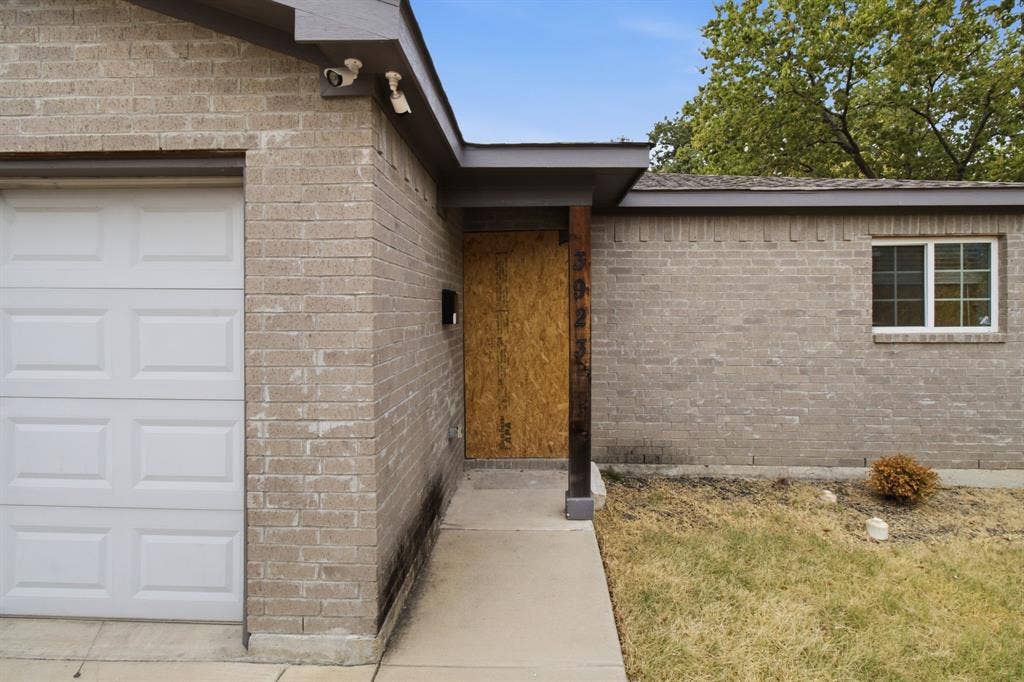 3923 Metropolitan Avenue, Dallas, TX 75210 Brick exterior with an attached garage featuring a panel door, covered entryway, and a window with white framing