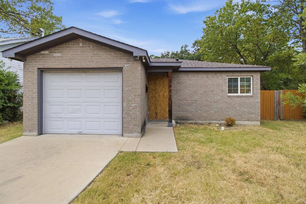 3923 Metropolitan Avenue, Dallas, TX 75210 Brick exterior featuring a front-facing garage with a white door, concrete driveway, and a wood fence