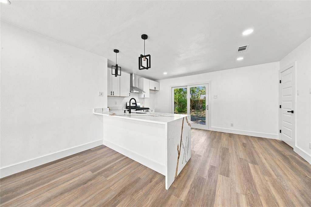 Open-concept living area with wood-finish flooring, a kitchen island with stone-finish countertop, and built-in white cabinetry