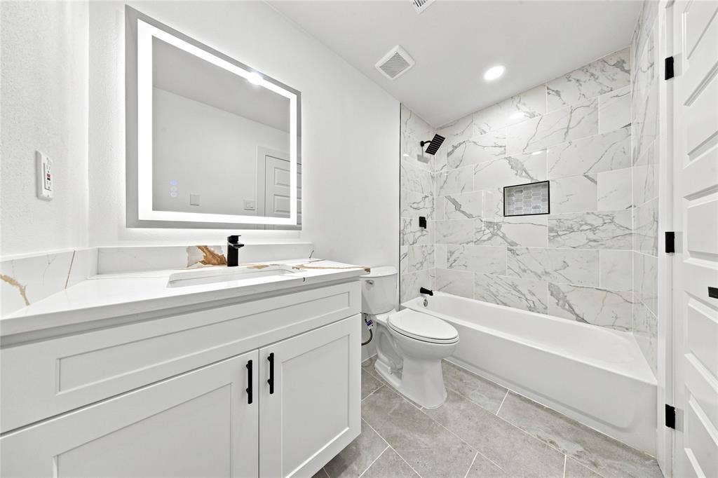 Modern vanity with integrated sink, backlit mirror, matte black fixtures, tiled shower surround, and a built-in shower niche