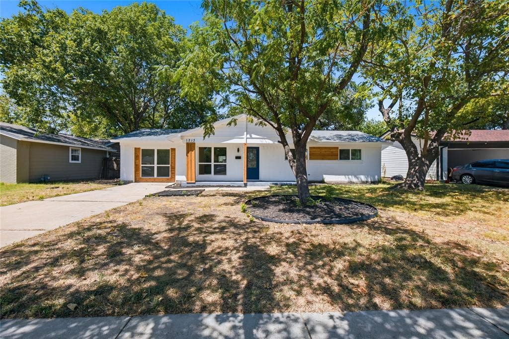 White exterior siding with a dark entry door, multiple large windows, wood-tone window accents, and a paved driveway
