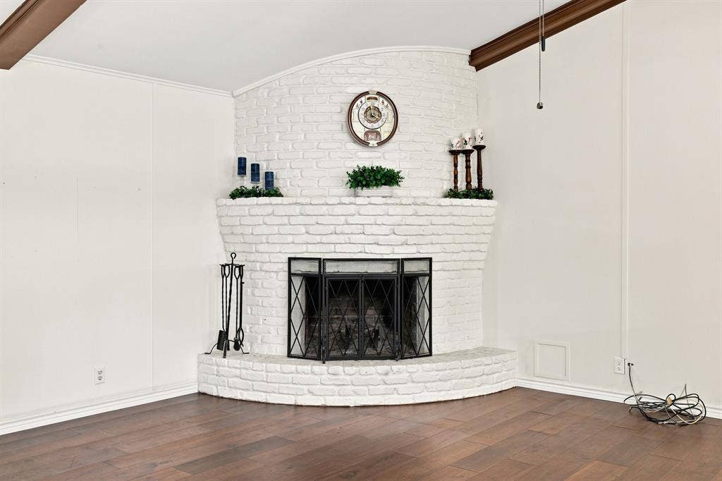 21121 County Road 1291, Flint, TX 75762 Corner fireplace with white painted brick surround and hearth, wood-finish flooring, and exposed wood beam