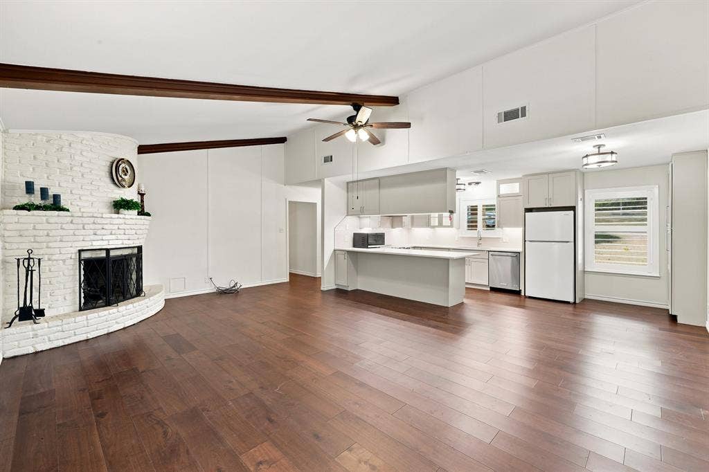 21121 County Road 1291, Flint, TX 75762 Open-concept living area featuring wood-finish flooring, a white-painted brick fireplace, an exposed beam ceiling, a ceiling fan, and recessed lighting in the kitchen area