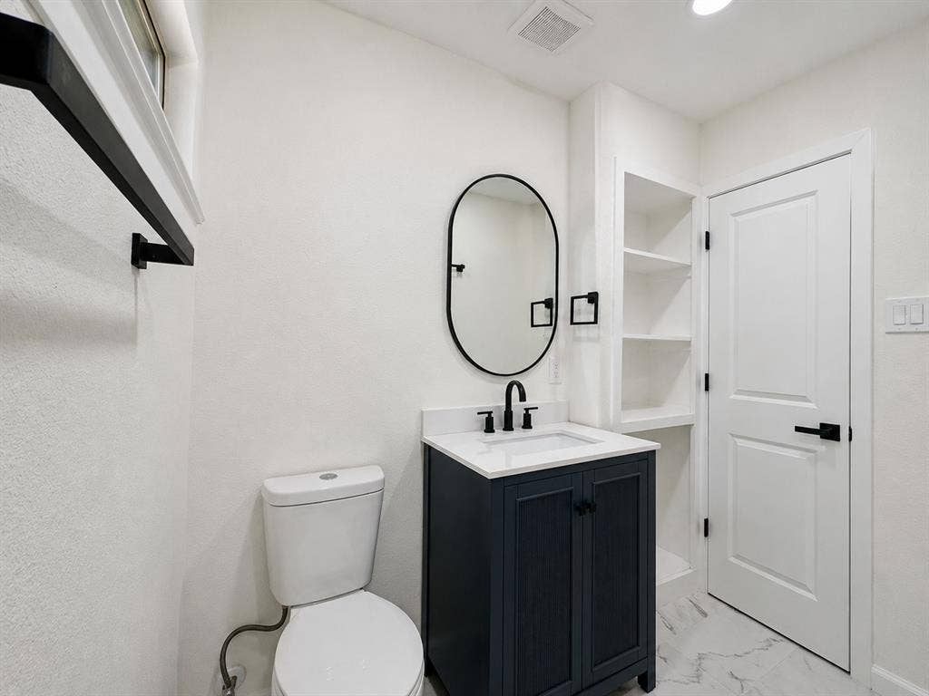 1842 Delmar Drive, Garland, TX 75040 Contemporary bathroom featuring a dark blue vanity with a white countertop, an oval mirror, and built-in shelving
