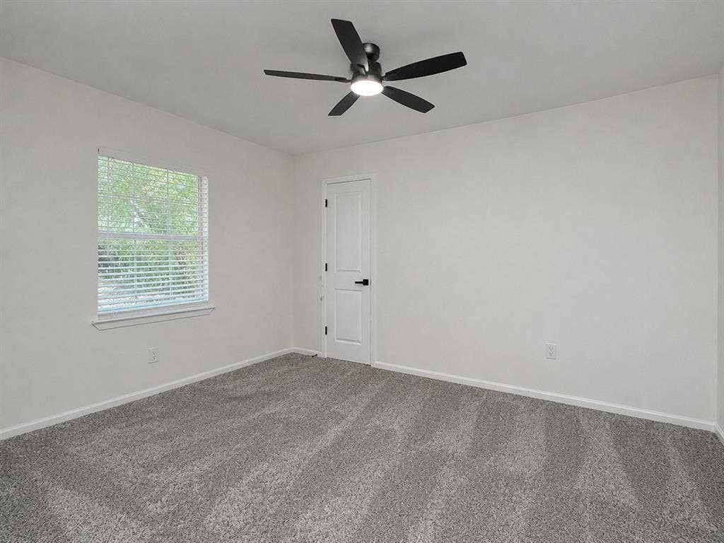 1842 Delmar Drive, Garland, TX 75040 Neutral wall color, grey patterned carpeting, contemporary ceiling fan with light, white door with black hardware, and window with blinds