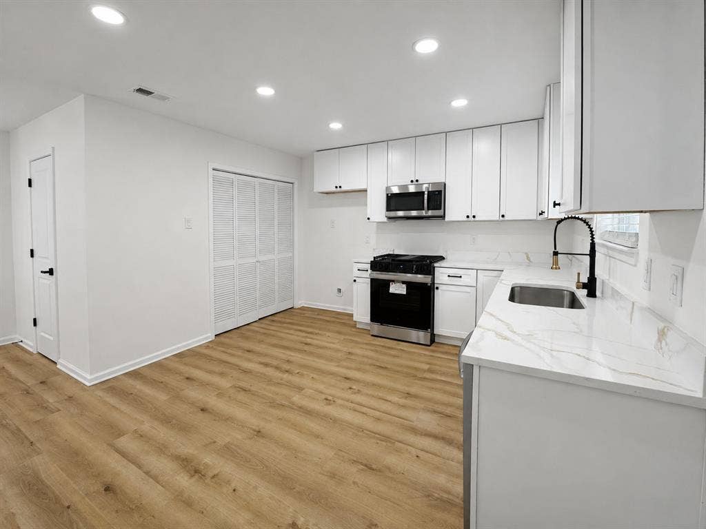 1842 Delmar Drive, Garland, TX 75040 Updated kitchen featuring wood-finish flooring, white cabinetry, integrated stainless steel appliances, and a marble-look countertop with a matching backsplash