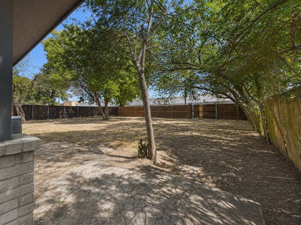 1842 Delmar Drive, Garland, TX 75040 Expansive outdoor space featuring a concrete patio, mature trees, and a full perimeter fence