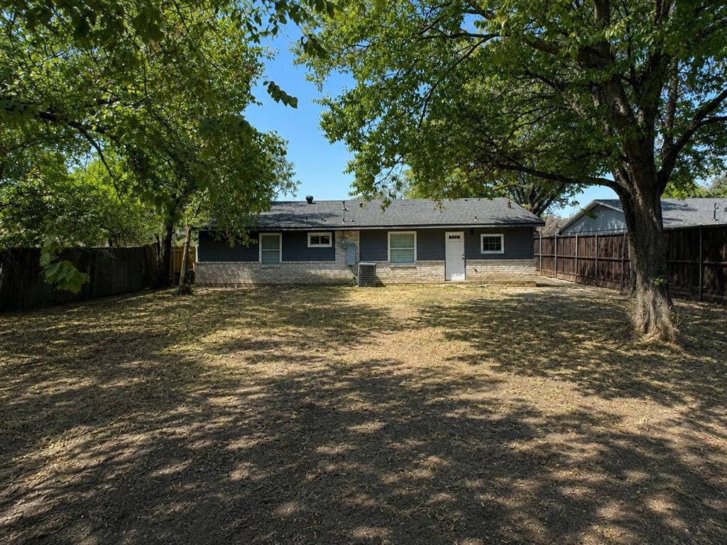 1842 Delmar Drive, Garland, TX 75040 Expansive backyard featuring mature trees, dark wood fencing, and a dwelling with stone and horizontal siding