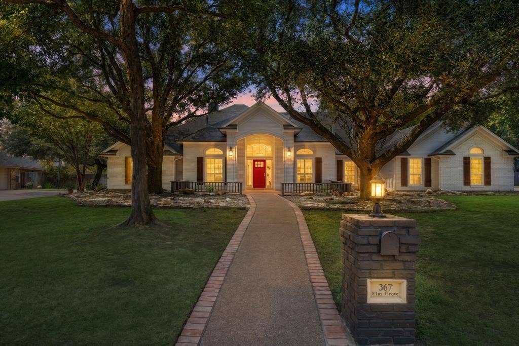367 Elm Grove Circle, Waco, TX 76657 White painted brick exterior with dark shutters, arched entry with a red door, stone landscaping, and a brick-edged pathway