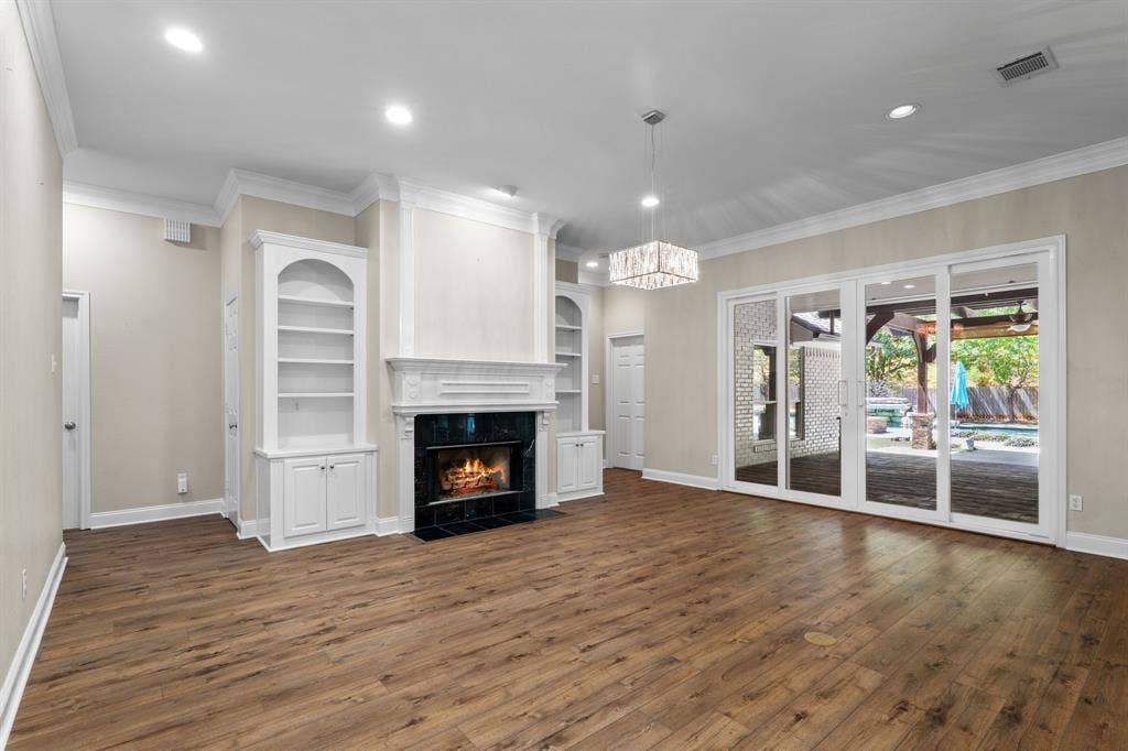 367 Elm Grove Circle, Waco, TX 76657 Wood-finish flooring throughout, featuring a fireplace with a dark-tiled surround and white mantelpiece, built-in shelving with lower cabinetry, and large sliding glass doors leading to an outdoor area