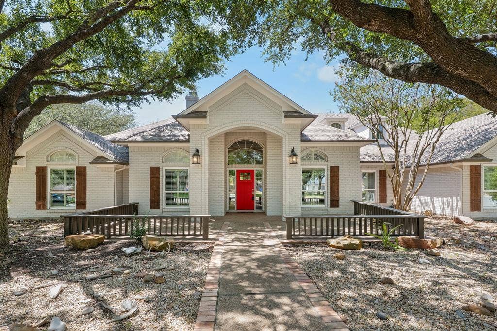 367 Elm Grove Circle, Waco, TX 76657 White brick exterior with a prominent red door, arched entry, decorative wood shutters, and exterior lighting fixtures