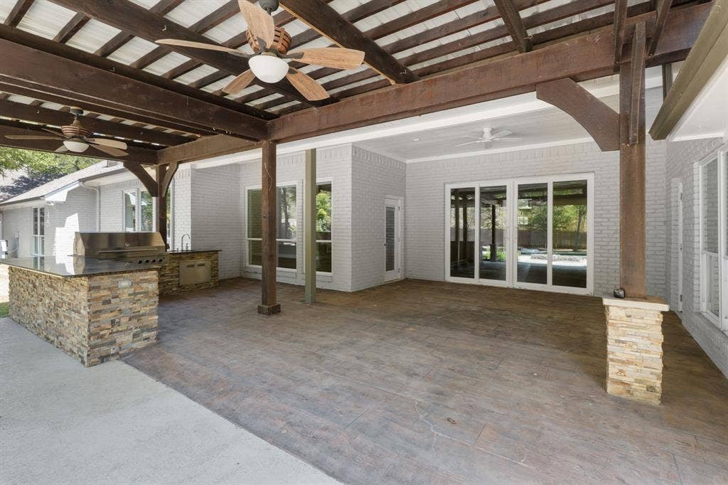 367 Elm Grove Circle, Waco, TX 76657 Covered patio featuring an outdoor kitchen with built-in grill, stone veneer accents, and a wood-beamed ceiling with ceiling fans