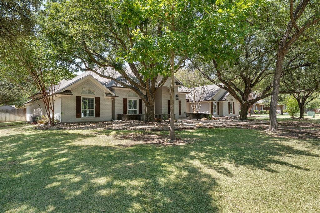 367 Elm Grove Circle, Waco, TX 76657 Spacious front yard with mature trees, stone landscaping, and a white exterior home with dark shutters