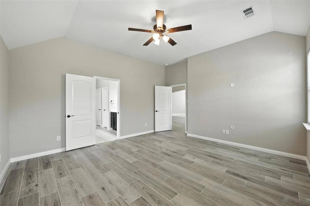 Vaulted ceiling featuring a ceiling fan with light fixture, wood-finish flooring, and white paneled doors