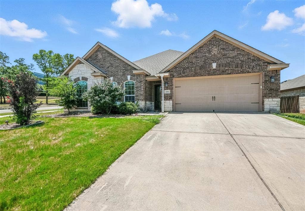Brick and stone facade, arched windows, attached two-car garage, concrete driveway, and front landscaping