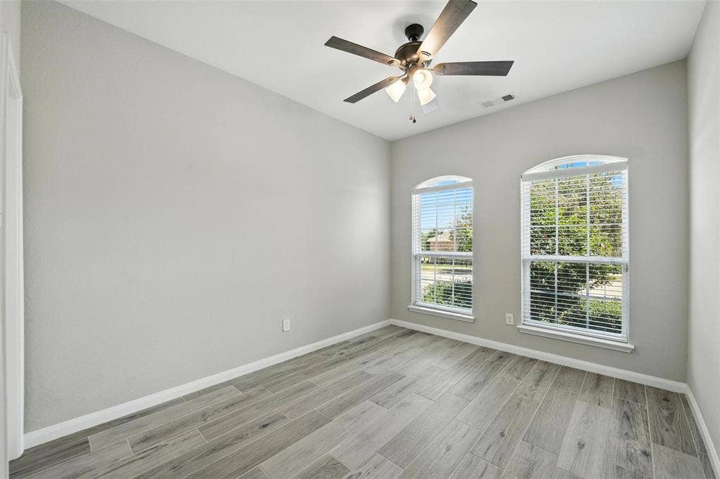 Vaulted ceiling featuring a ceiling fan with integrated lighting, two arched windows with blinds, and wood-finish flooring in the secondary bedroom