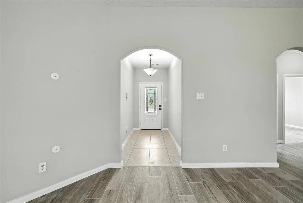 Archway entry with a front door featuring decorative glass, tile flooring, and wood-finish flooring