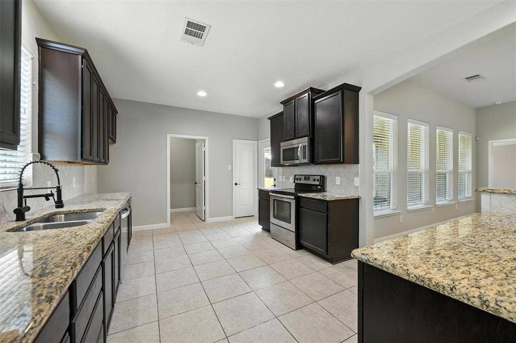 Kitchen featuring dark wood cabinetry, granite countertops, stainless steel appliances, and tile flooring