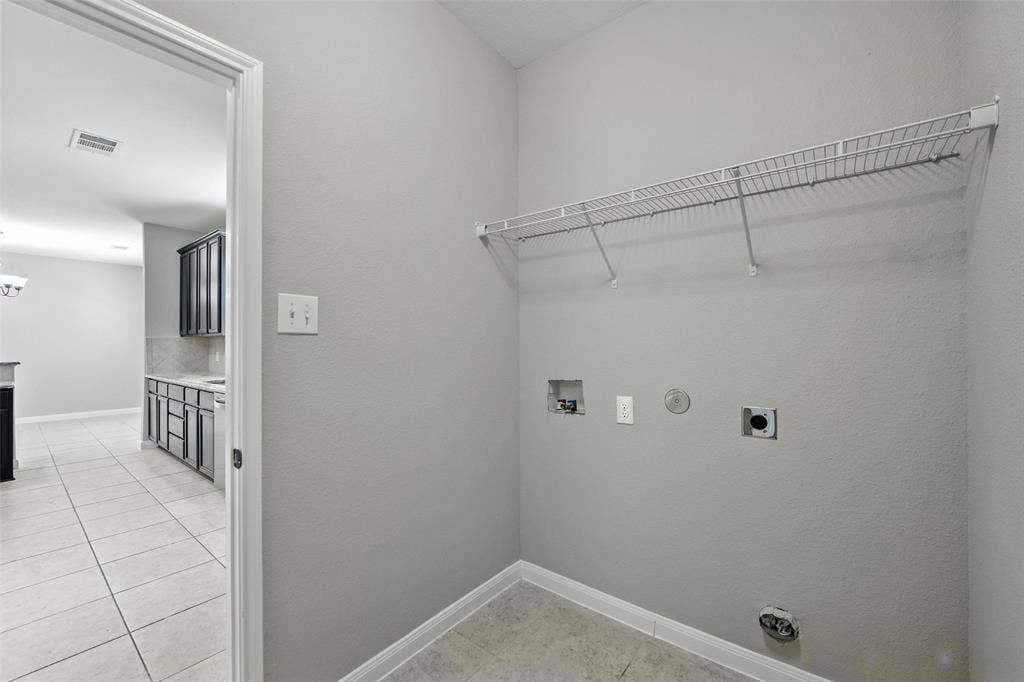 Laundry area with a wire storage shelf, utility hookups, and tiled flooring