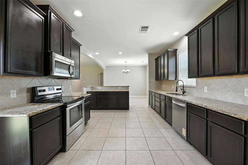 Kitchen featuring dark wood-finish cabinetry, light-toned countertops, stainless steel appliances, tile flooring, and a tile backsplash