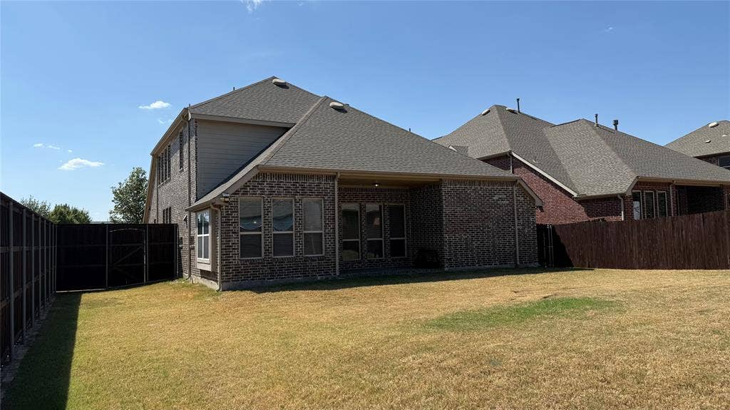 Brick exterior with a covered patio, multiple windows, and a dark wood fence enclosing the perimeter