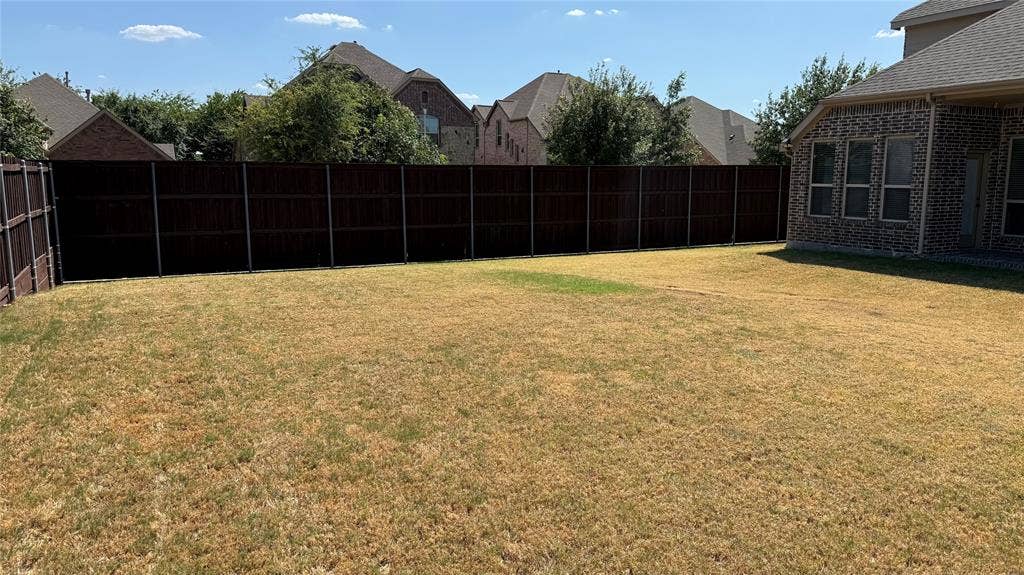 Expansive lawn area with a perimeter wood fence, complementing the brick exterior of the property