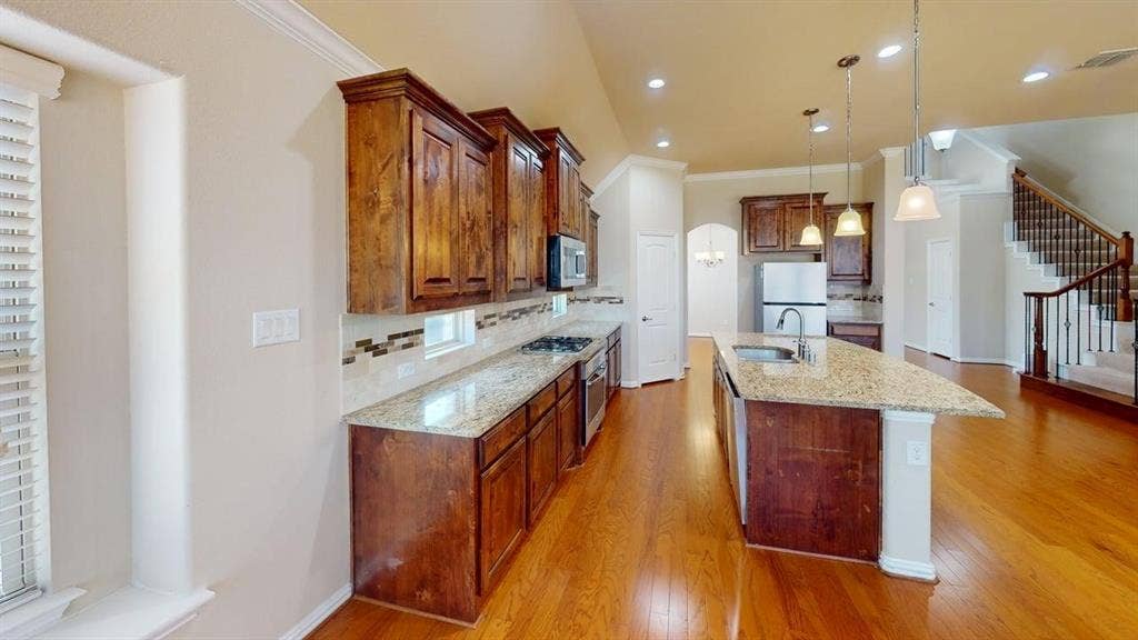 Wood-finish flooring throughout, kitchen with stone countertops, wood cabinetry, stainless steel appliances, and an island with pendant lighting