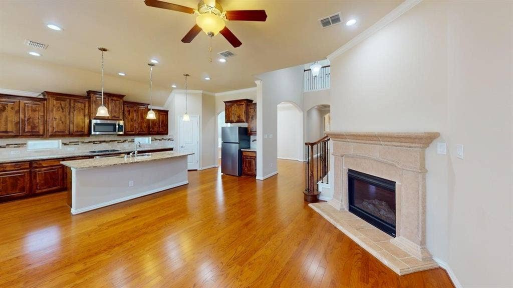 Hardwood flooring throughout, kitchen island with pendant lighting, stone fireplace, stainless steel appliances, and wood cabinetry