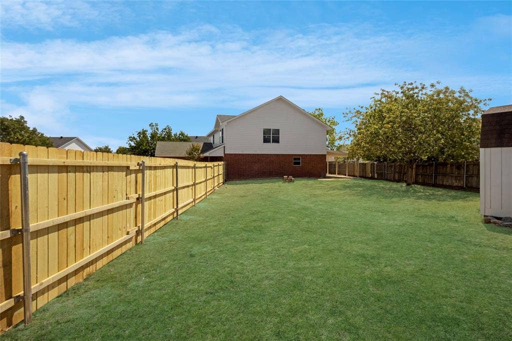 408 Centennial Place, Crowley, TX 76036 Expansive grassy yard with wood privacy fencing, a storage shed, and a two-story residence with brick and siding exterior