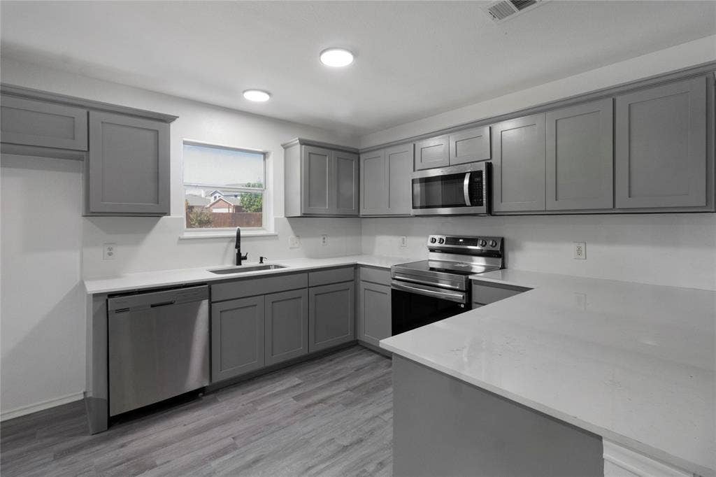 408 Centennial Place, Crowley, TX 76036 Kitchen featuring gray shaker-style cabinetry, stainless steel appliances, white countertops, a stainless steel sink with a black gooseneck faucet, and wood-finish flooring