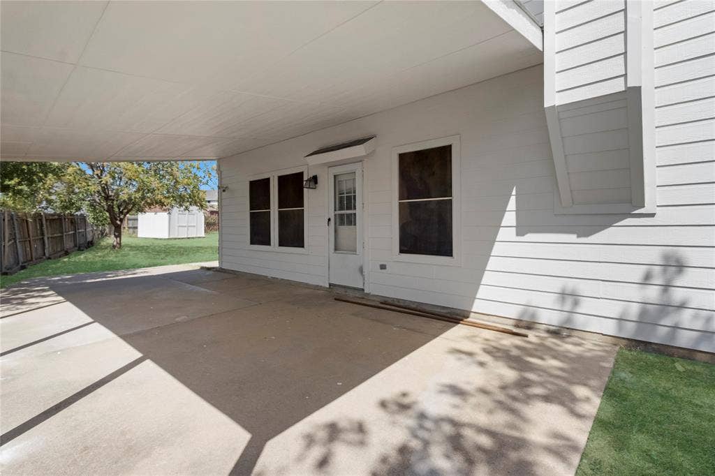 408 Centennial Place, Crowley, TX 76036 Covered concrete patio with a white paneled exterior, leading to a fenced yard with a detached shed