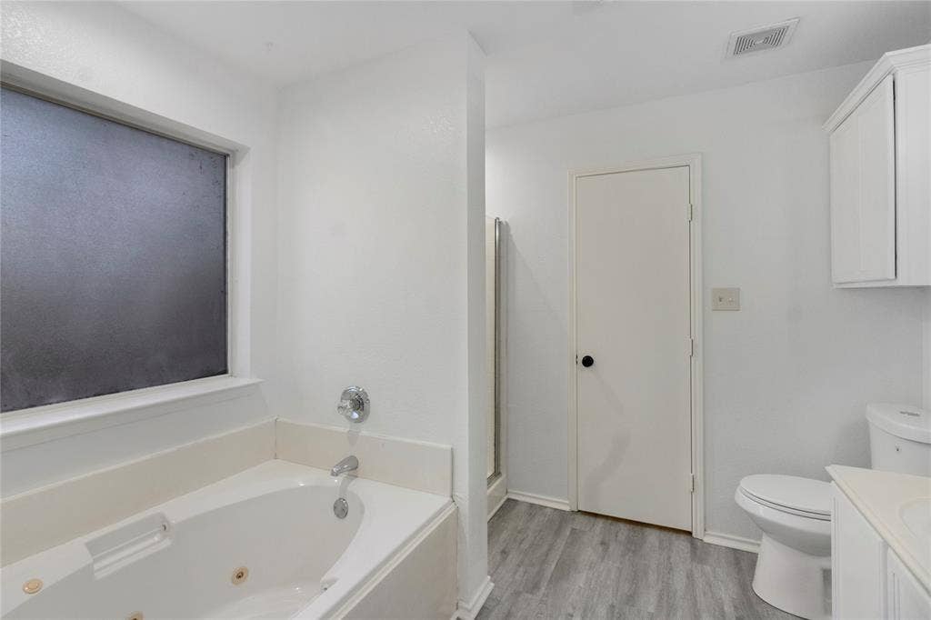408 Centennial Place, Crowley, TX 76036 White jetted tub with chrome fixtures, frosted window, and wood-finish flooring