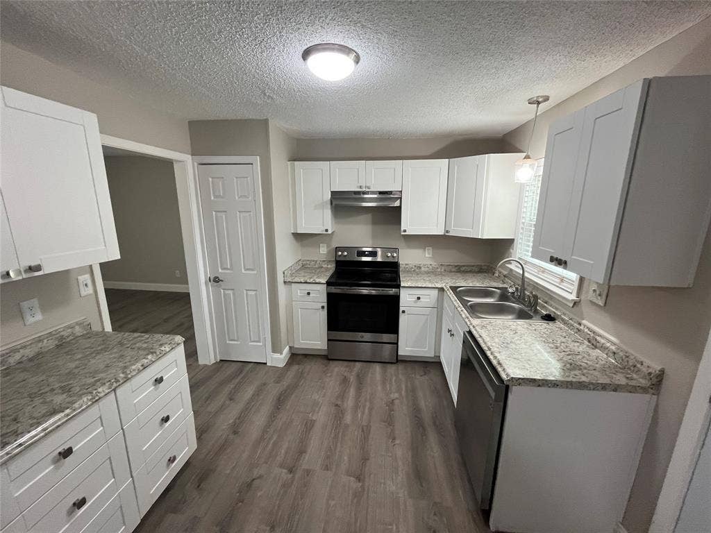 820 E Edith Street, Irving, TX 75061 Modern kitchen featuring white shaker-style cabinetry, stainless steel appliances, granite-look countertops, a double basin sink, and wood-finish flooring
