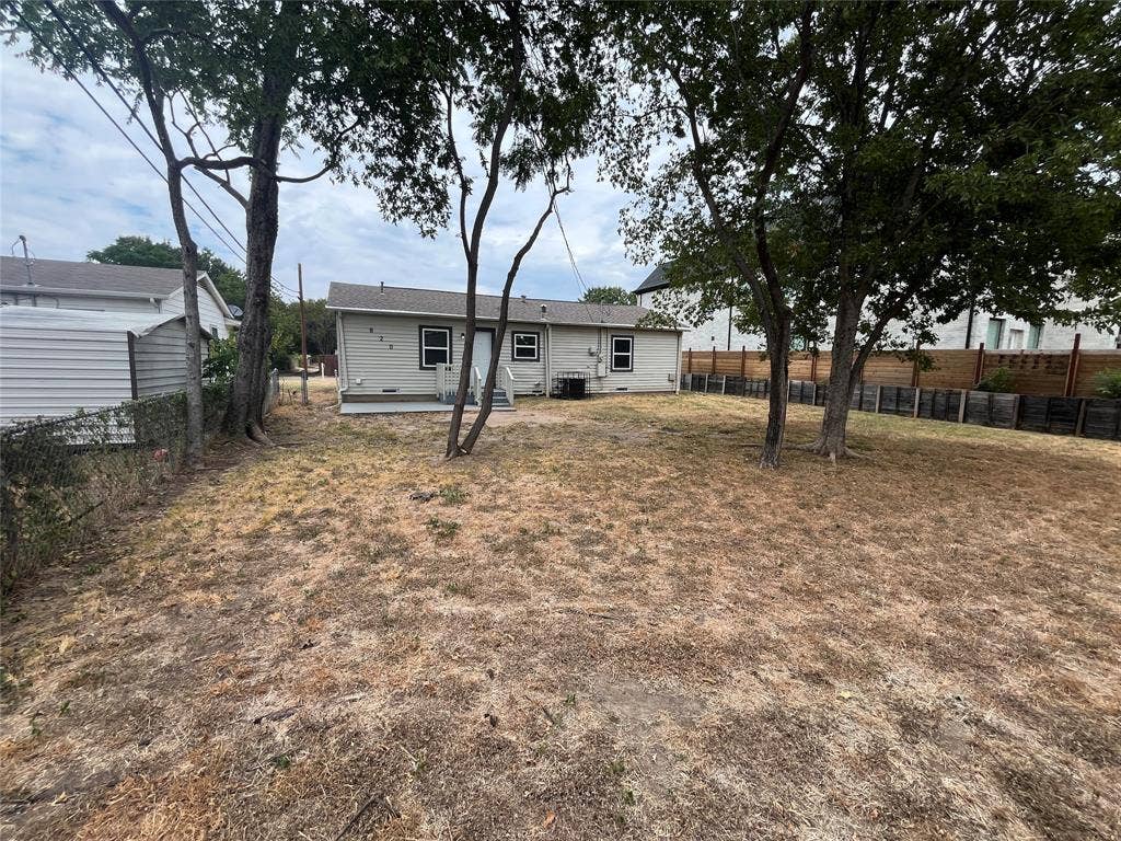 820 E Edith Street, Irving, TX 75061 Expansive backyard with mature trees and a chain-link fence, featuring a back concrete patio