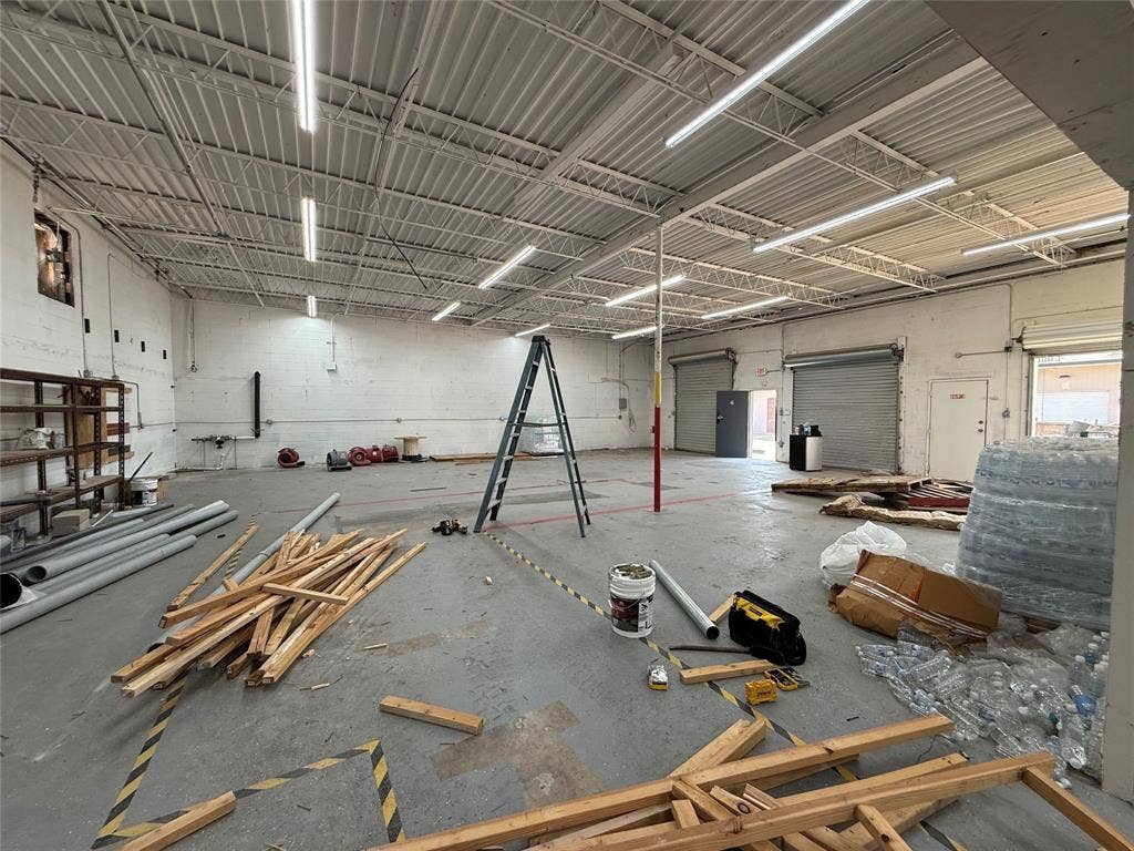 4309 Action Street, Garland, TX 75042 Spacious commercial interior featuring a high trussed ceiling, multiple fluorescent light fixtures, two roll-up doors, and an additional personnel door